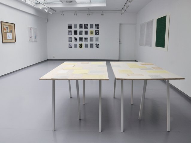 Overview of installation with works on paper arranged on two tables. Photography.